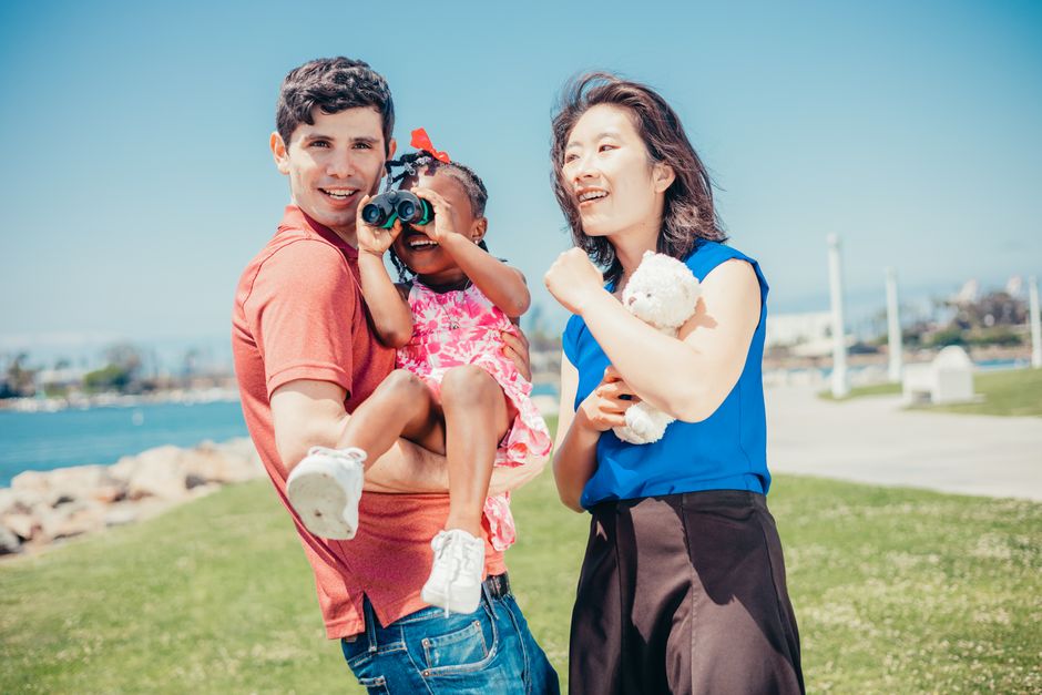 Joyful family enjoying time outdoors with a child using binoculars on a sunny day.