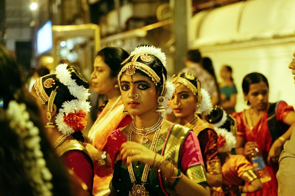 A vibrant street scene of Bharatanatyam dancers in traditional attire at night in Guruvayur, India.