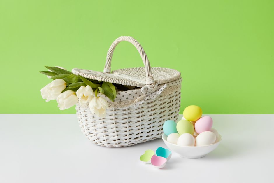 White wicker basket with tulips and pastel eggs on bright green background, perfect for Easter themes.