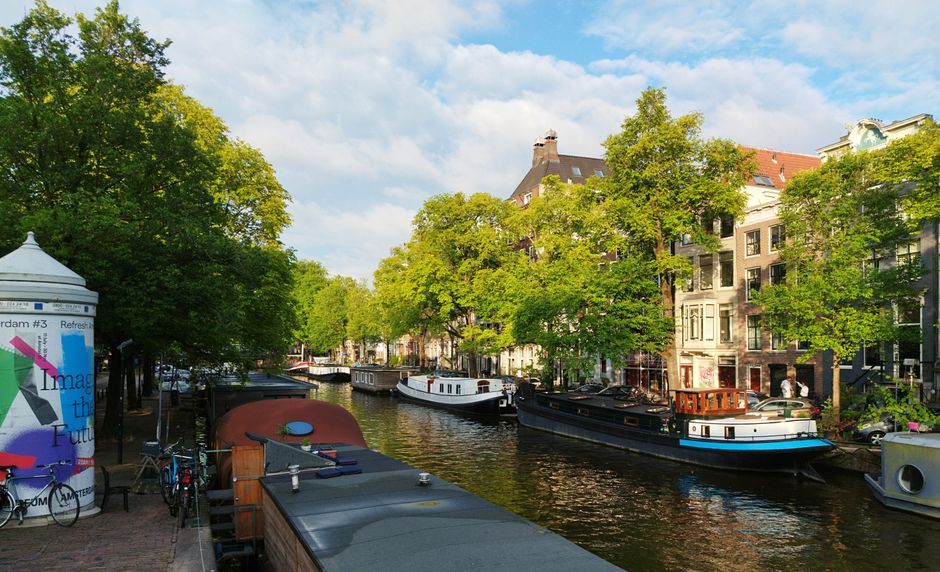 Scenic view of Amsterdam's iconic canal with houseboats and lush trees on a sunny day.