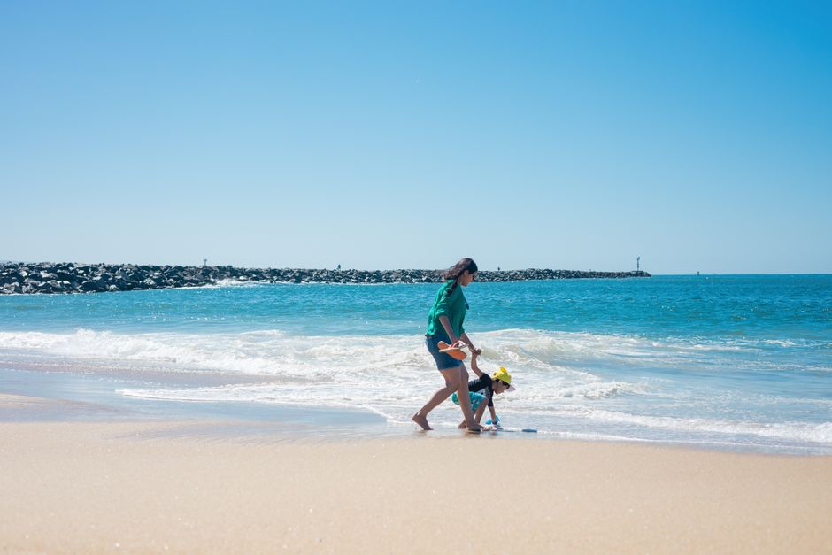 Mother and child enjoying a sunny day playing on the sandy beach by the ocean.