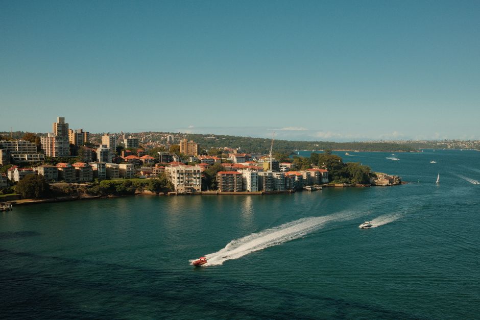 Scenic aerial view of Sydney's coastal architecture and waterways with boats in motion under a clear blue sky.