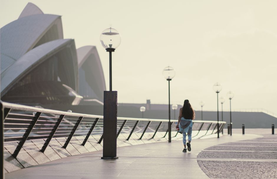 A woman walks along the promenade near Sydney Opera House on a sunny day.