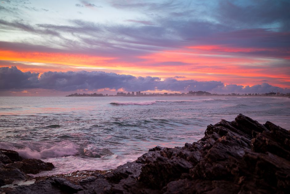 Stunning sunset view over Currumbin coastline with rocks and waves under a colorful sky.