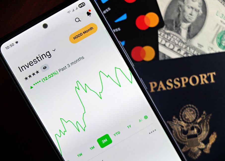 Smartphone showing stock market app with travel essentials: passport, money, and cards.