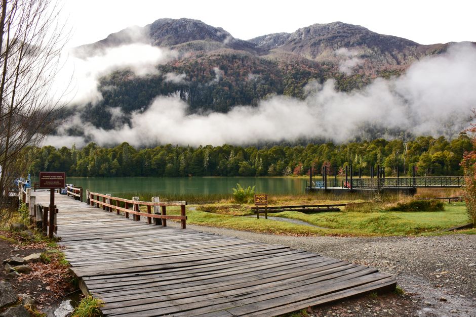 Tranquil scene of a mountain lake with a wooden dock and misty forests.
