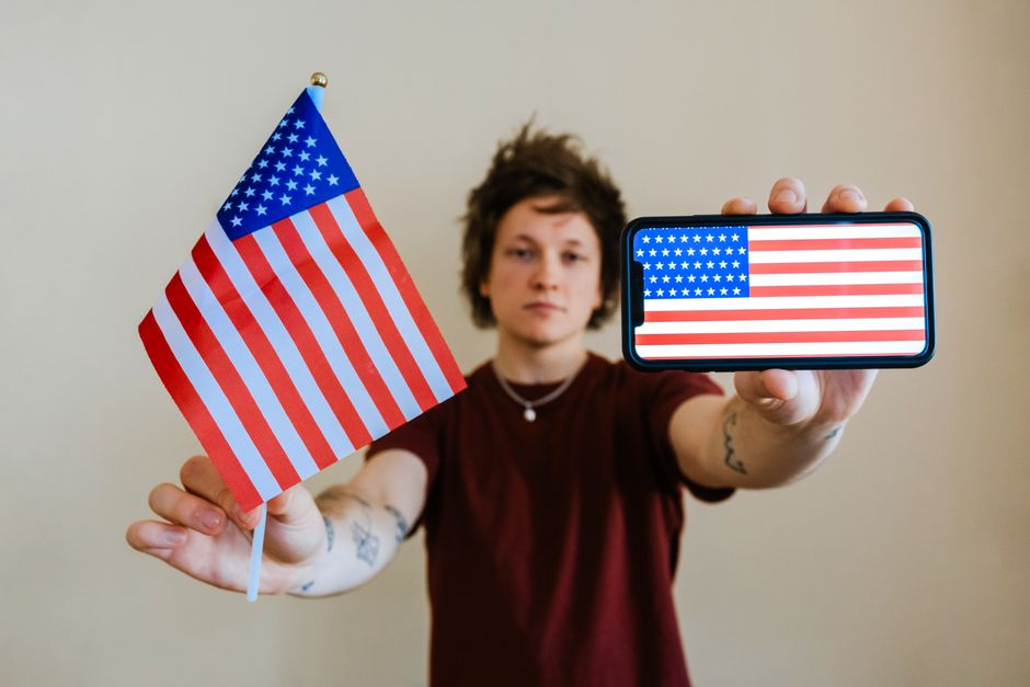 Person displaying American pride with flag and smartphone showing USA flag.
