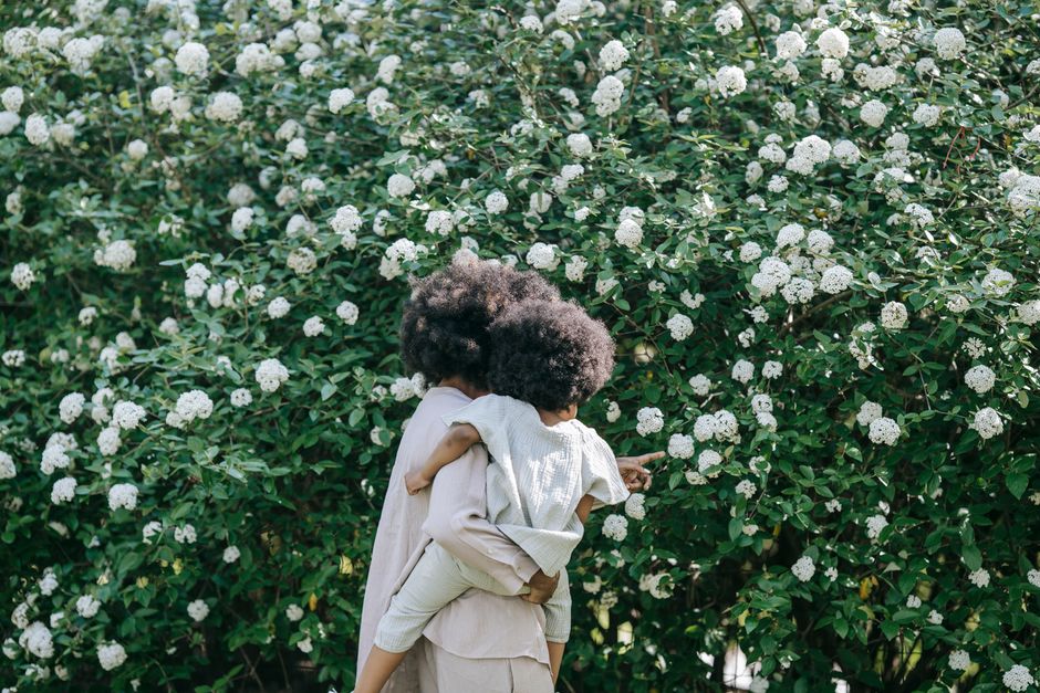 A mother carrying her child in front of a lush flowering shrub, a moment of love and nature.