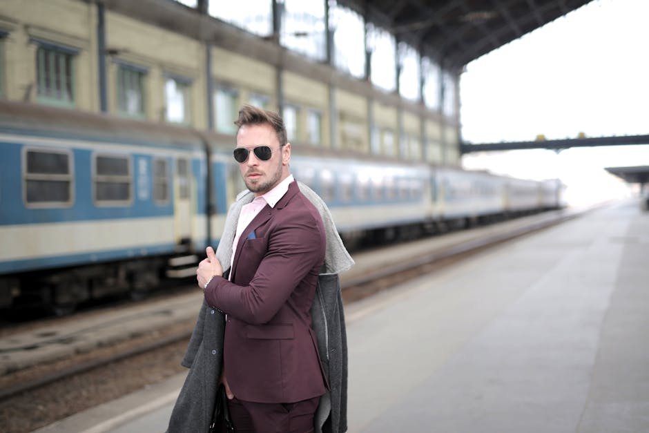 A fashionable man stands at a train station in a suit, waiting for the train.