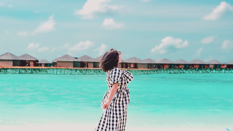 A woman relaxes on a tropical beach with turquoise waters and overwater bungalows in the Maldives.