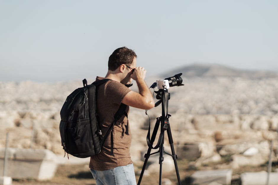 A focused photographer takes pictures outdoors with a DSLR camera on a tripod.