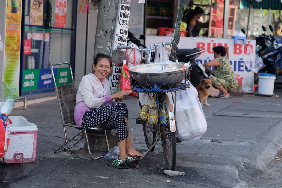 Happy woman street vendor selling food from a bicycle cart on a bustling city sidewalk.