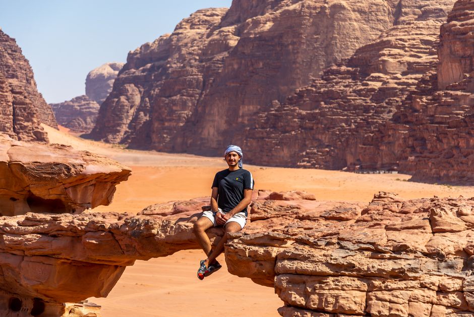 Person enjoying a scenic view atop a natural rock bridge in Wadi Rum, Jordan's vast desert landscape.
