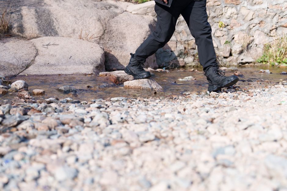 A person crosses a rocky stream outdoors, showcasing hiking gear and rugged terrain.