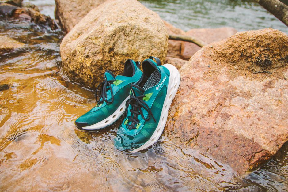 Pair of green sneakers submerged in a rocky stream, showcasing waterproof design.